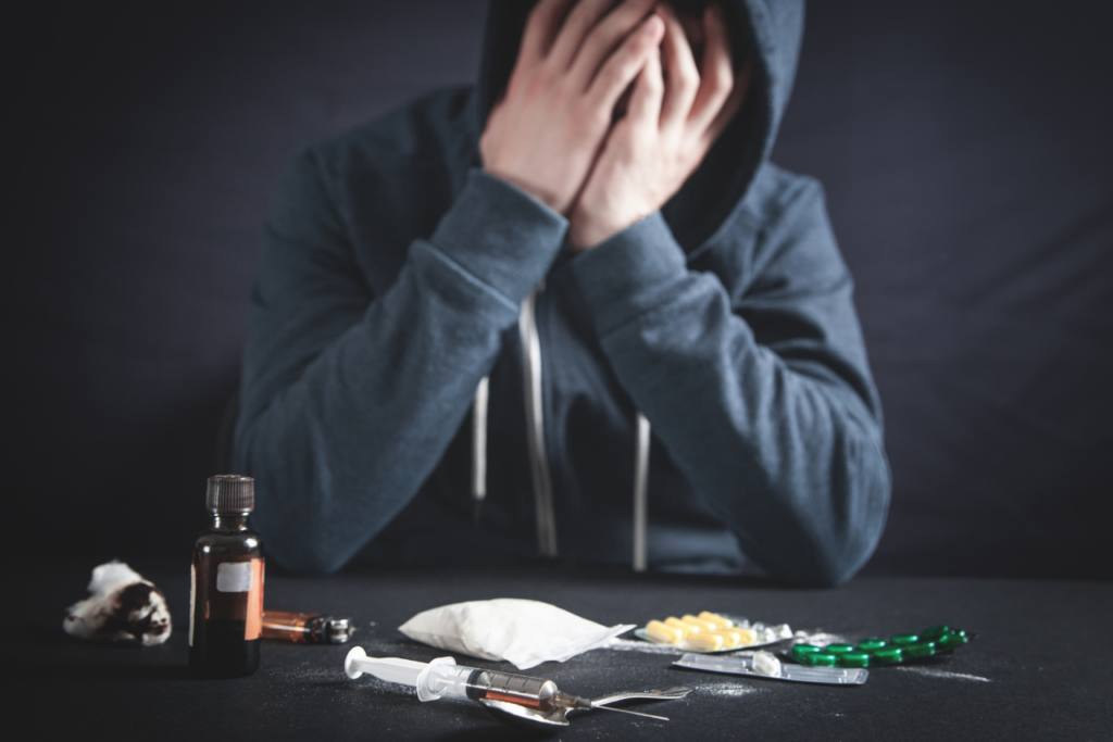 man sitting at a table that has several different types of drugs on it wondering how many days to break an addiction